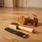 Brosse pour semelle daim posée sur un parquet de danse, à côté d'une sandale de danse latine en satin caramel